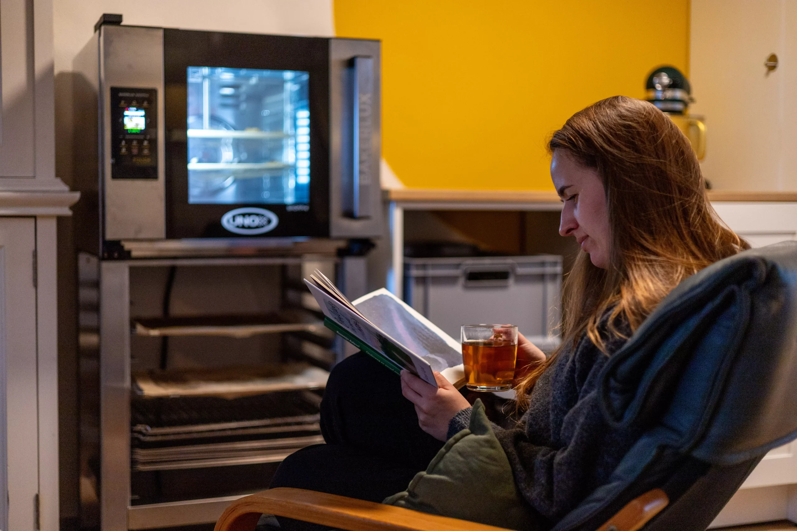 Muriël zit met een kopje thee te lezen voor een oven vol verse koekjes.